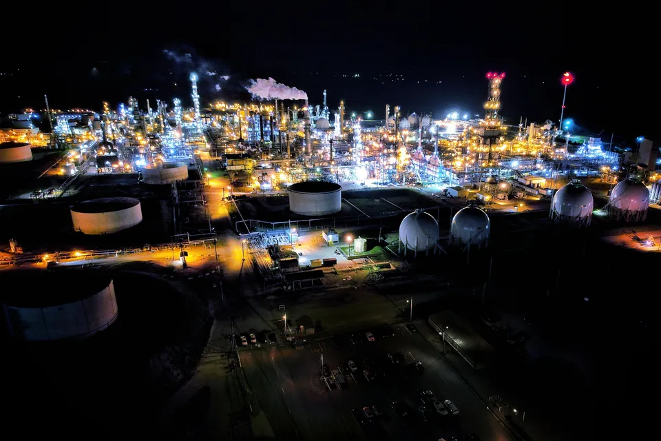 A striking view of an industrial facility in Zuid-Holland, illuminated at dusk against a clear blue sky.